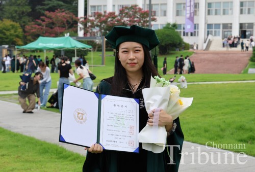 A graduate poses for a photo in front of the library building after the graduation ceremony on August 26.