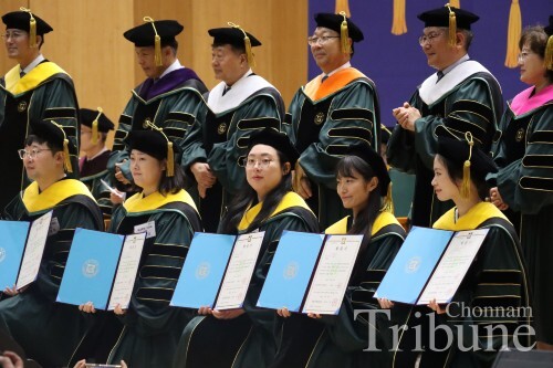 Graduates awarded their doctoral degree certificates pose for a picture with the professors.