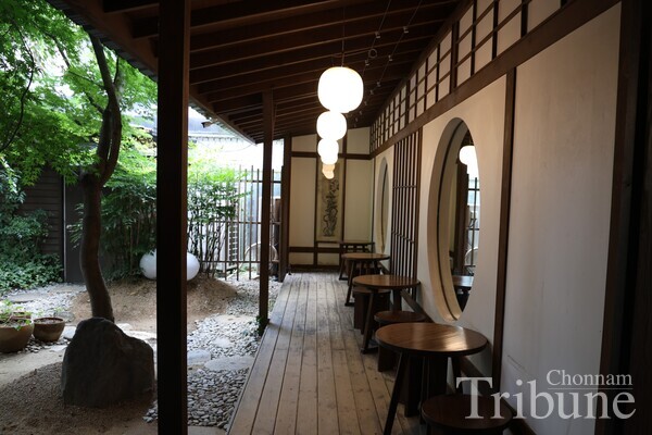 The serene outdoor seating area offers a peaceful retreat with wooden architecture, round mirrors, and a lush garden view, blending nature and design.