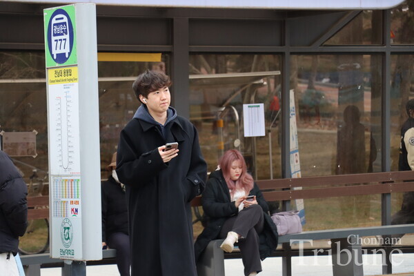 A student checks his phone while waiting for the bus.