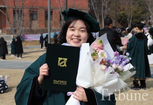 A graduating student poses for a picture showing her diploma at Bongji Field on Feb. 26.