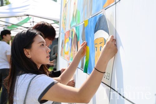 A student attaches his own painted section to a multi-panel canvas to complete memorial artwork on May 12.