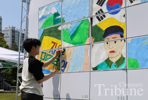 A student attaches his own painted section to a multi-panel canvas to complete memorial artwork on May 12.