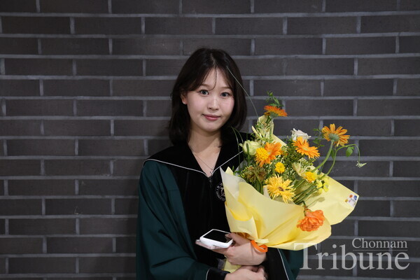 A graduate poses holding a flower inside the College of Humanities.